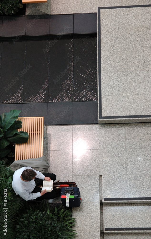 man reading with luggage in airport