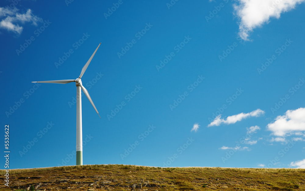 Wind turbine on top of hill against blue sky background