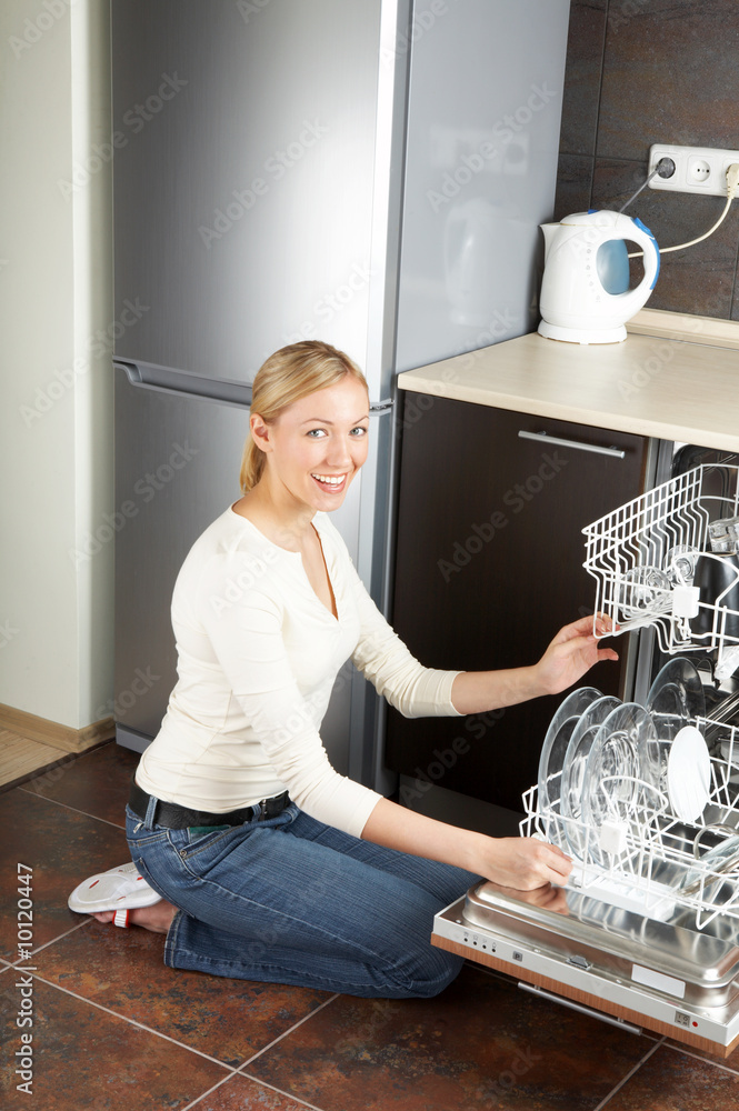 The blonde sits near to the open dishwasher on kitchen