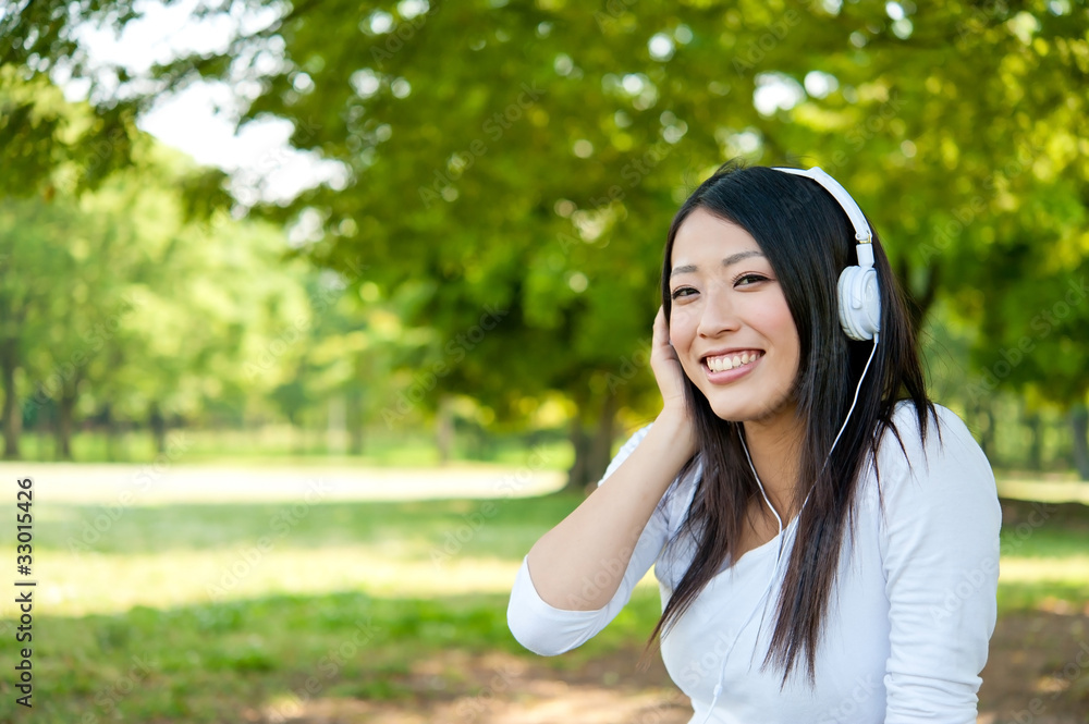 美丽的亚洲女人在公园里听音乐