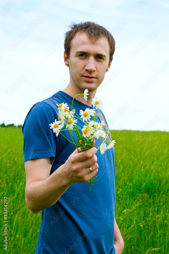 The young man with camomiles on a green meadow