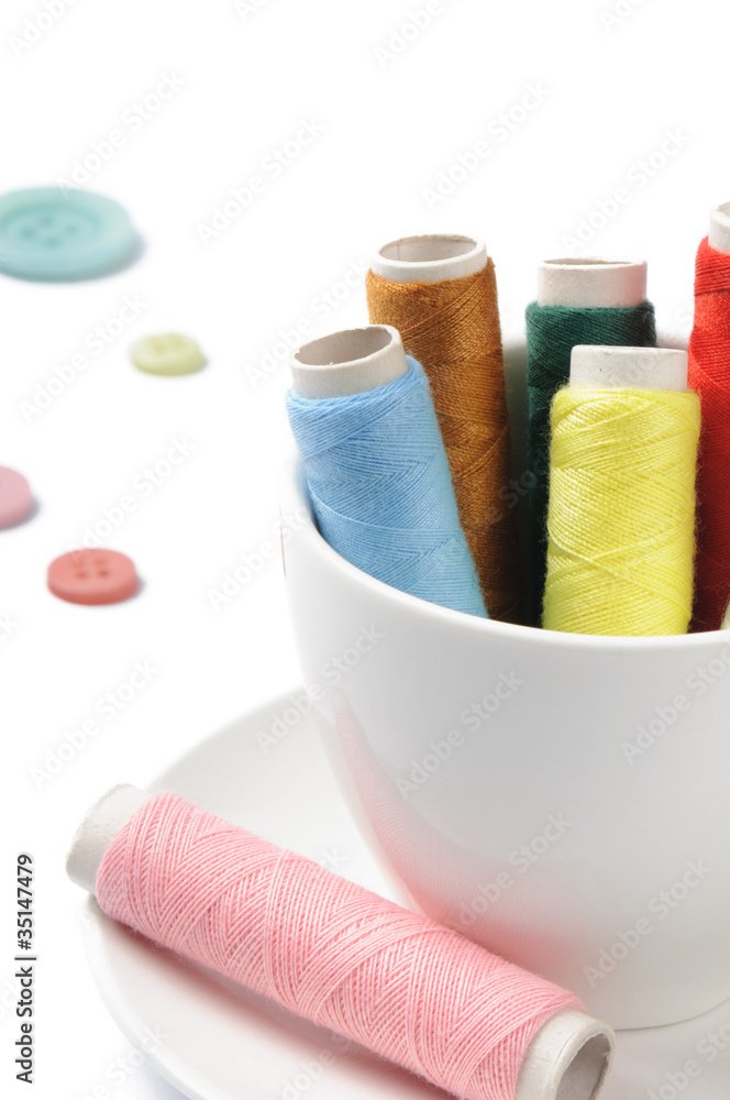 Colorful bobbins in a cup over white