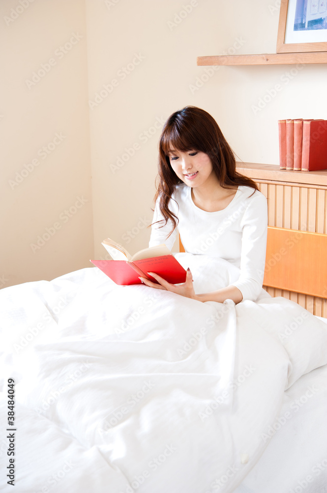 attractive asian woman reading a book on the bed