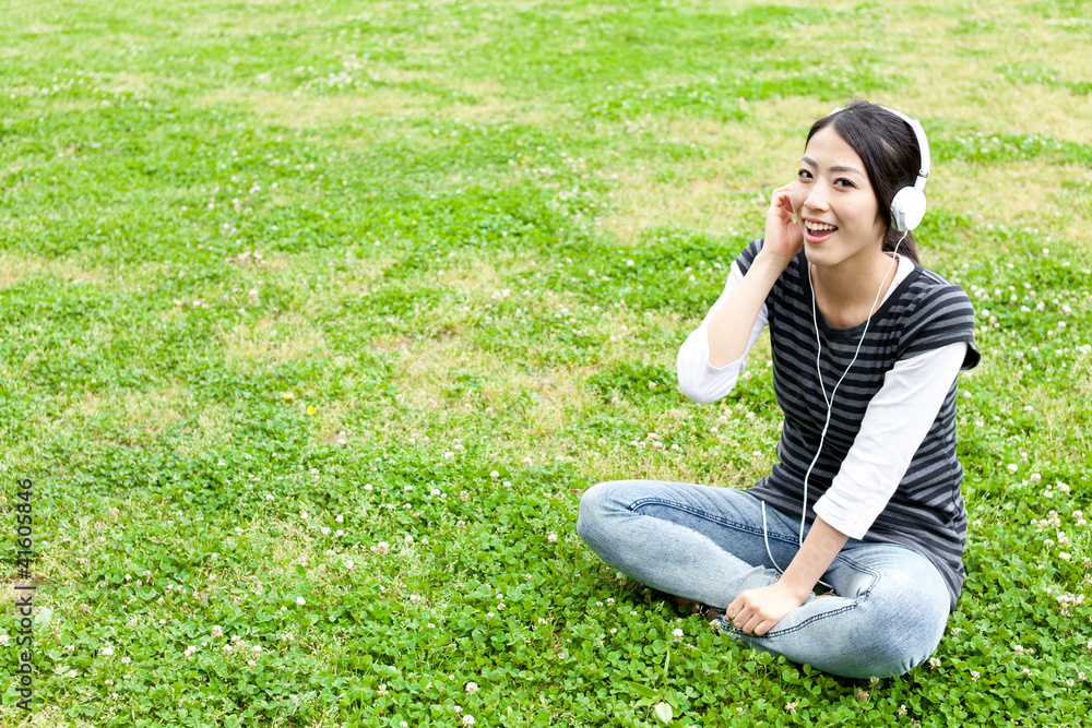 迷人的亚洲女人在公园里听音乐