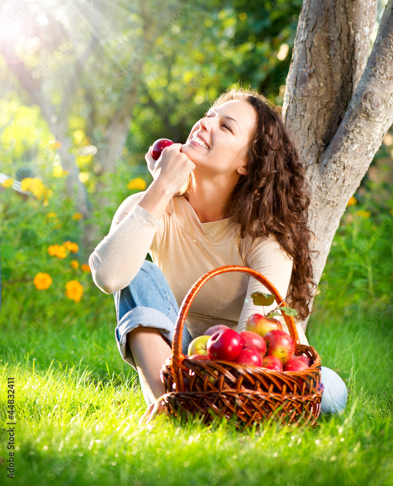 Happy Smiling Young Woman Eating Organic Apple in the Orchard