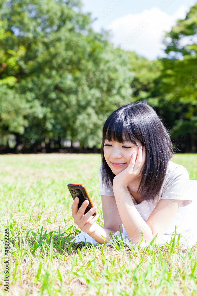 漂亮的亚洲女人在公园里使用智能手机