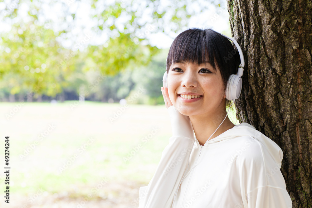 迷人的亚洲女人在公园里听音乐