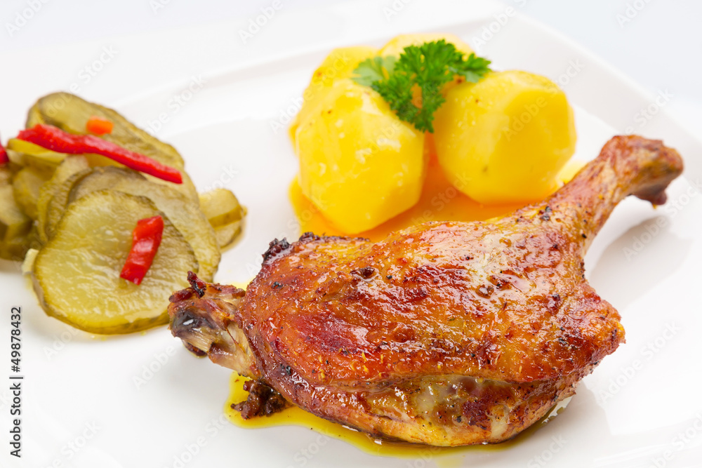 Roast duck leg with potatoes and pickes on the plate