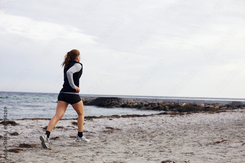 Young female runner running on beach