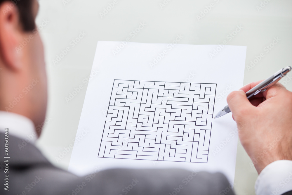 Businessman Looking At Maze Puzzle Holding Pen