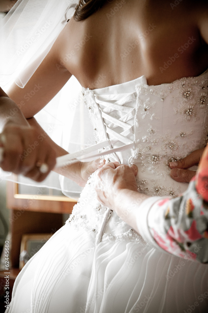 Closeup shot of bridesmaid tying corset on bridal dress