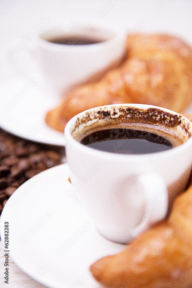 Two ceramic cups of black coffee and croissants