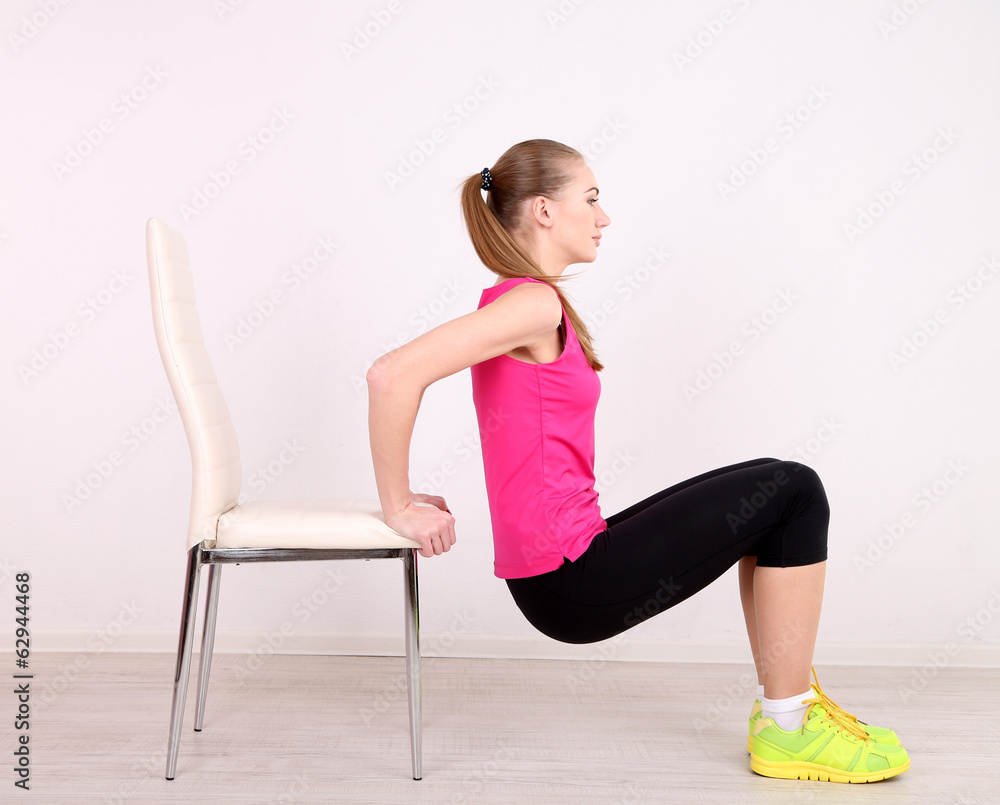 Young beautiful fitness girl exercising with chair in gym