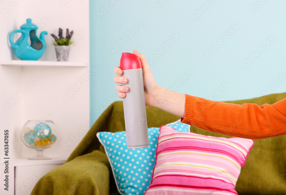 Sprayed air freshener in hand on home interior background