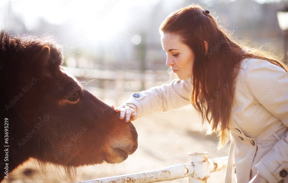 Young woman stroking pony in mini zoo