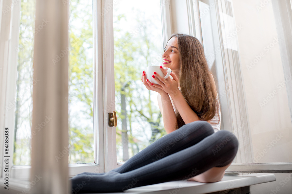 Young and cute lady sitting on the windowsill and looking out th