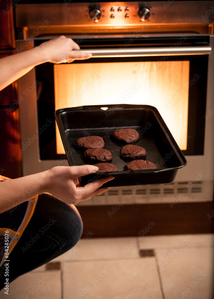 photo of housewife putting pan with cookies in oven