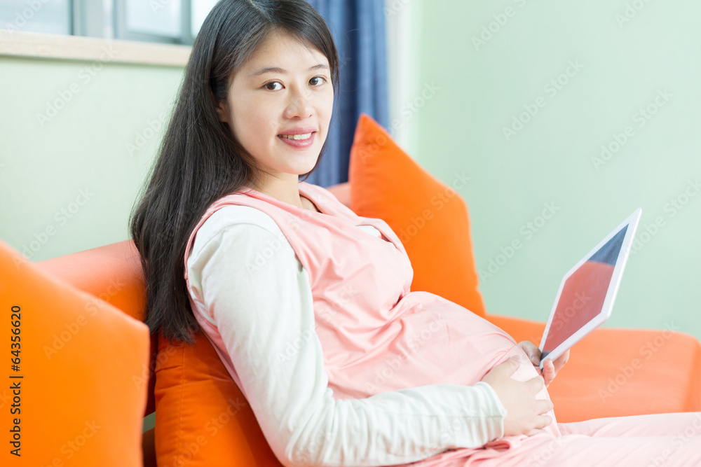 Happy pregnant woman looking at camera, using a digital tablet