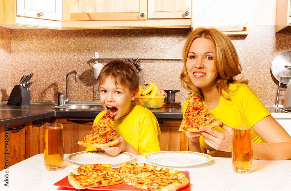 Hungry boy and his mother eating pizza in kitchen