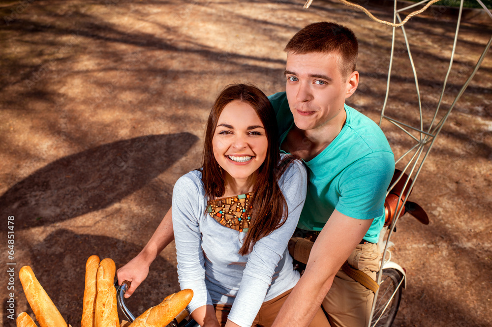 Young and joyful couple having fun in the park with bicycle and