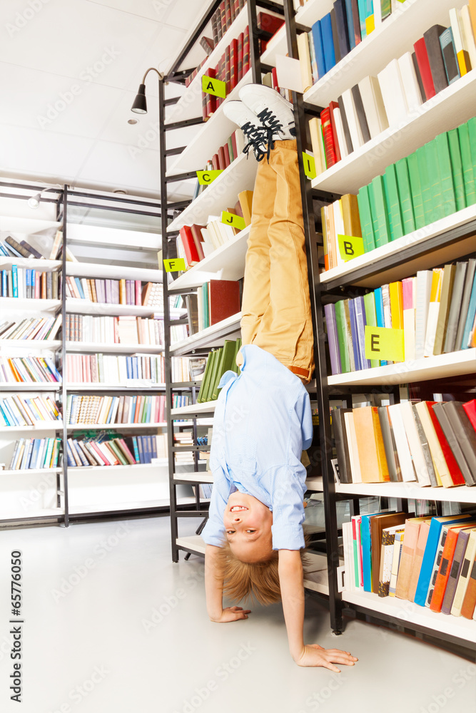 Boy standing on arms upside down in library