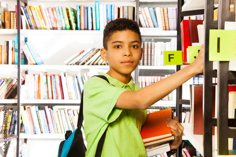 Serious boy looks and searches book on shelf