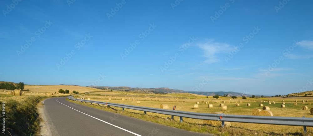 Strada asfaltata con colline e rotoballe