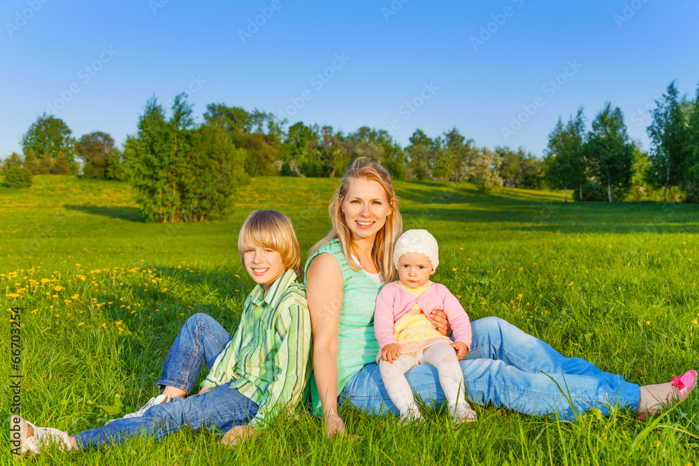 Mother with kids sits on grass in park