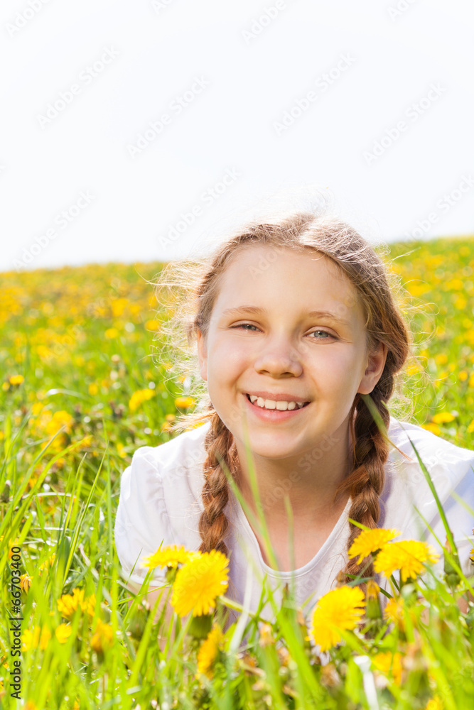 Smiling girl laying in dandelions meadow