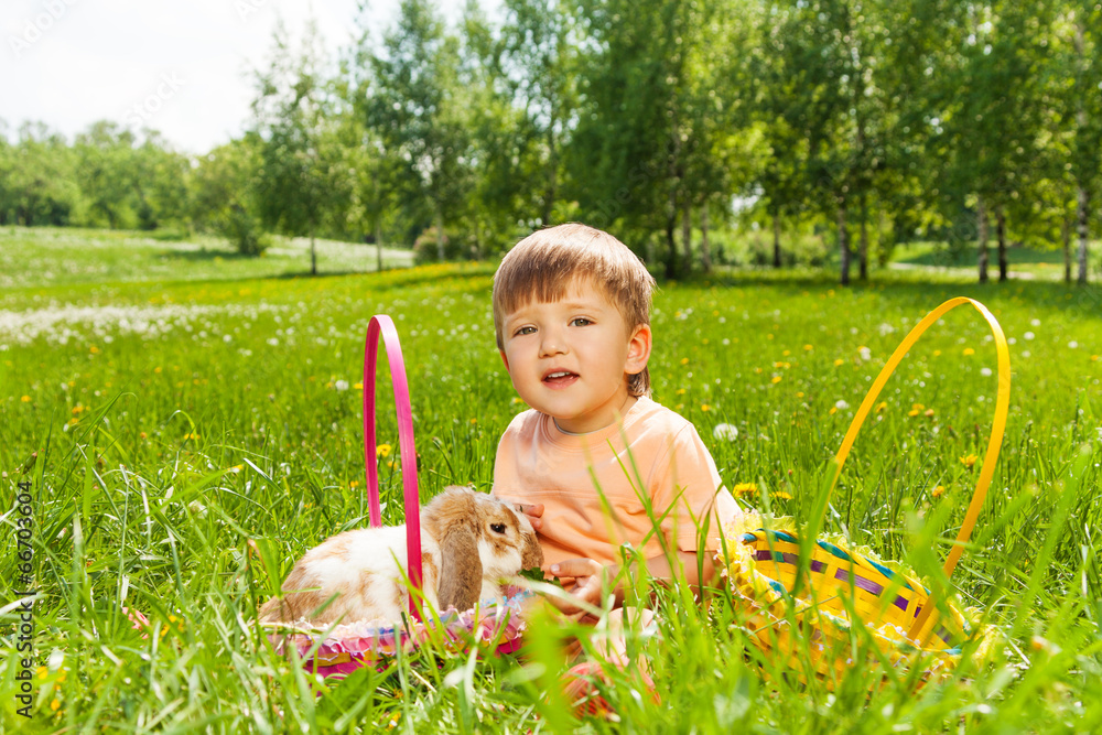 Smiling boy with rabbit and baskets on the grass