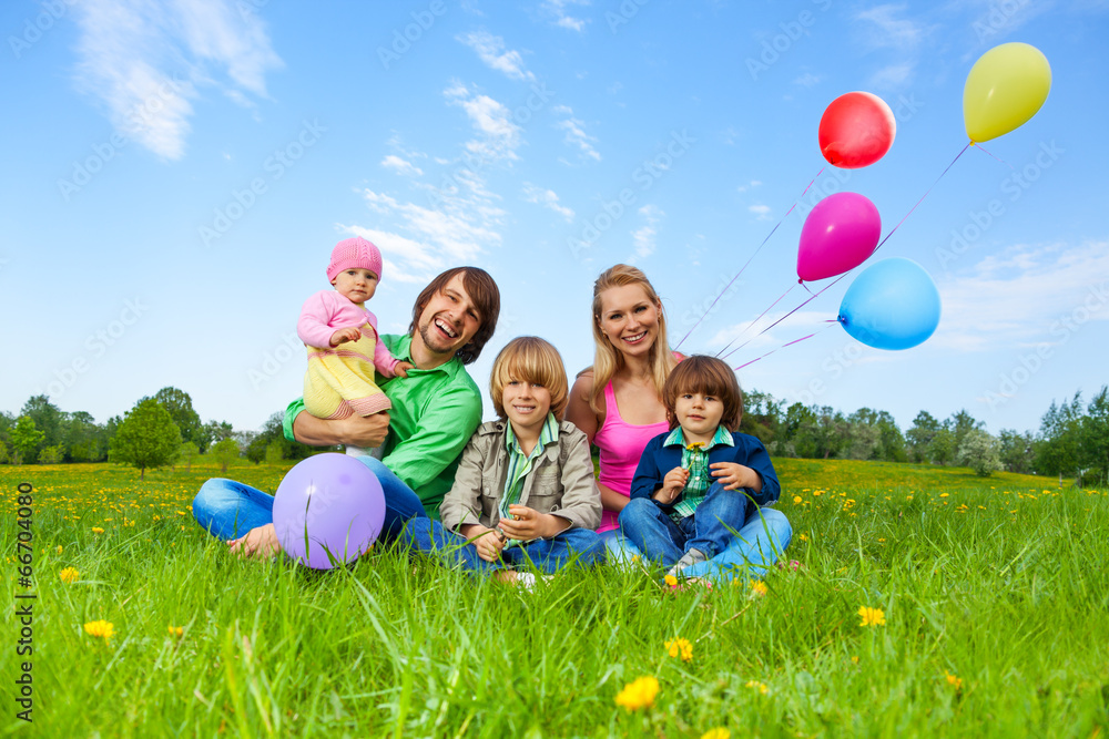 Smiling family sitting on grass with balloons