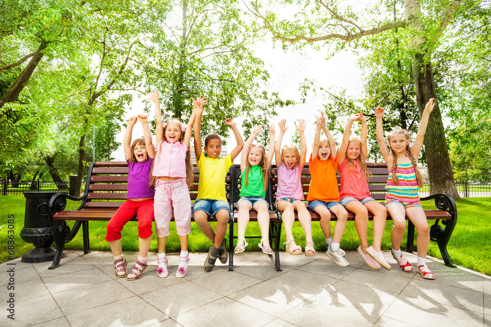 Excited kids with arms and sit in row on bench