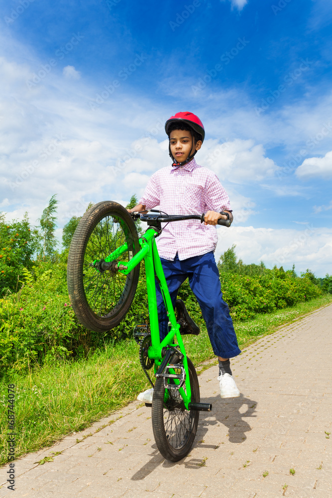 African boy with one wheel of bike up rides it