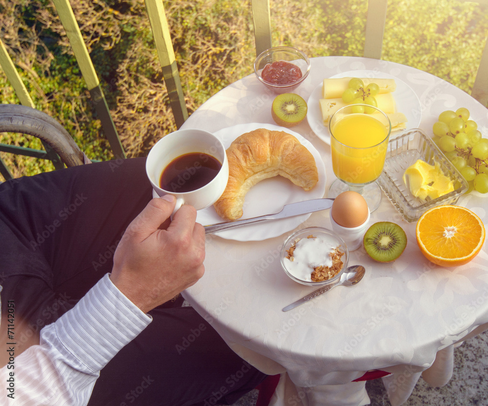 Mann trinkt Kaffe am Frühstückstisch auf dem Balkon