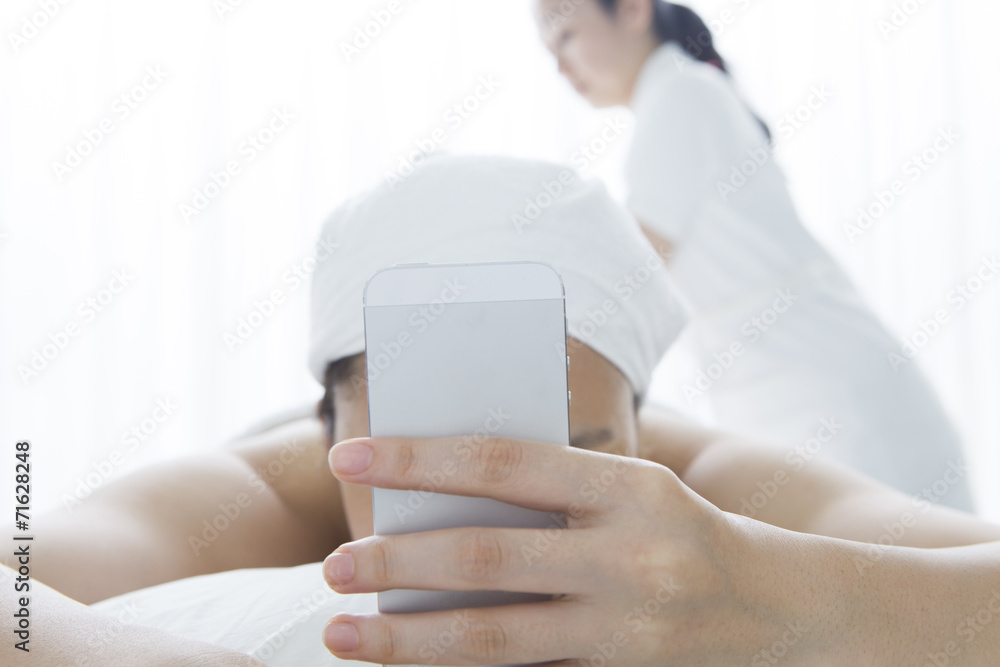 Young woman looking at the mobile phone while getting a massage