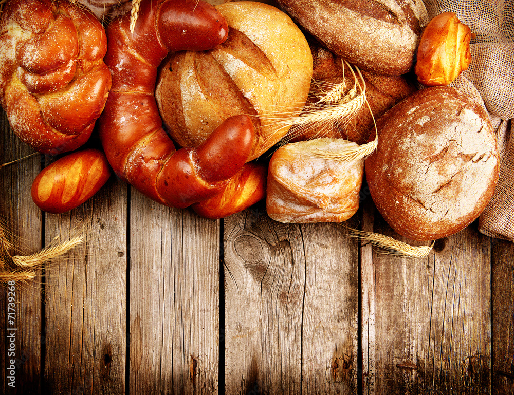 Various Bread and Sheaf of Wheat Ears over Wood Background