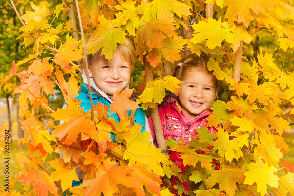 Girl and boy hiding in yellow autumn leaves