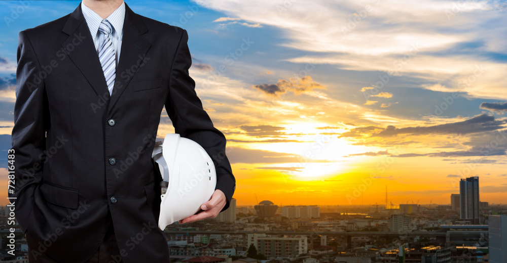 Businessman holding safety helmet with city background