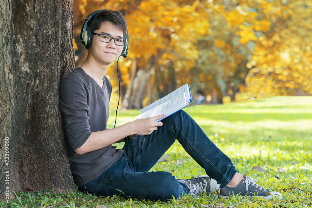 英俊的学生在公园里听音乐