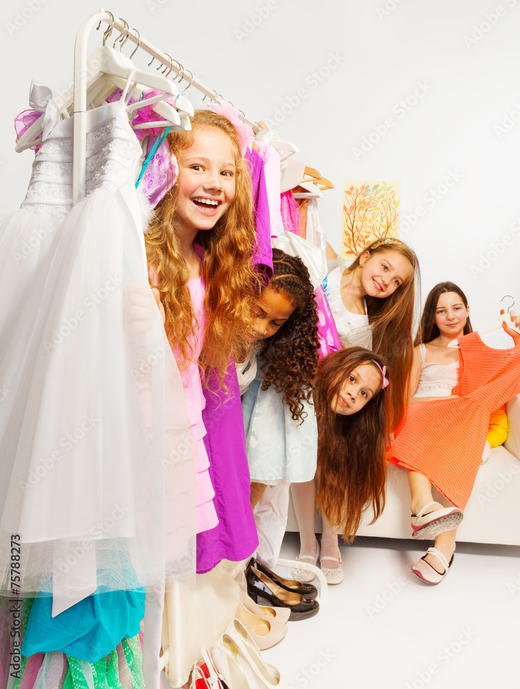 Positive girls during shopping behind hangers