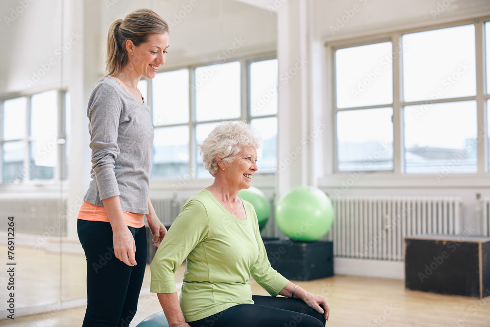 Female instructor assisting senior woman exercising in gym