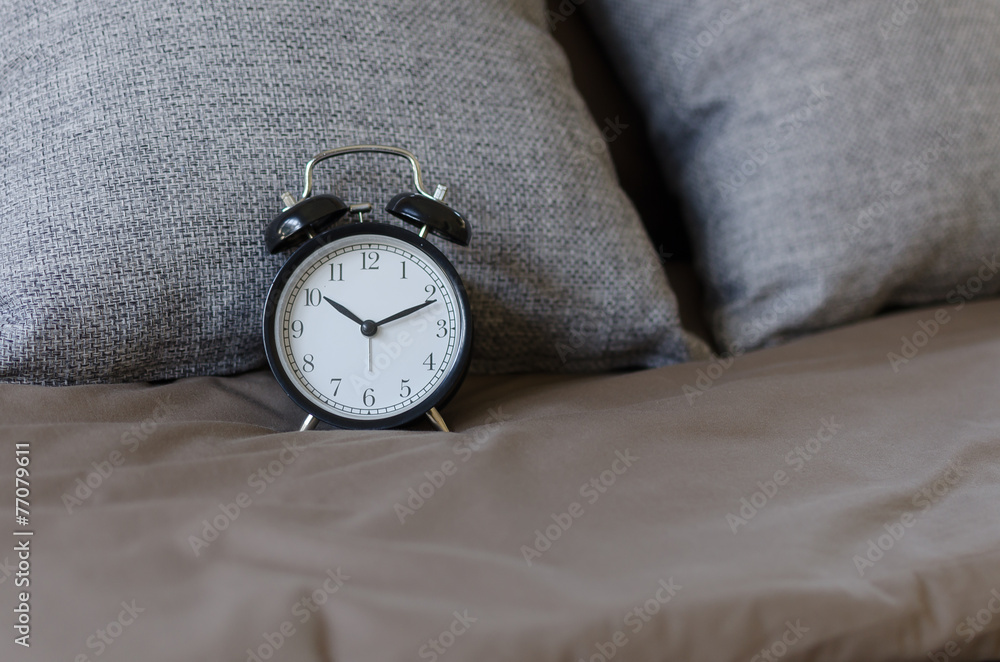 black alarm clock on brown bed with grey pillow