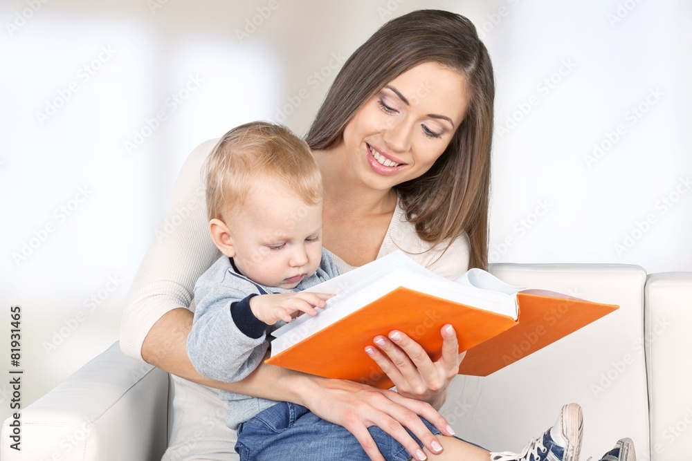 Adult. Mother reading a book a little baby daughter on the sofa