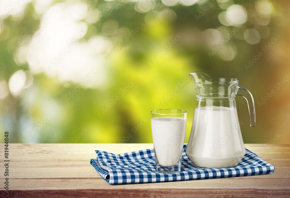 Milk. A glass of milk and a milk jug on plaid tablecloth.