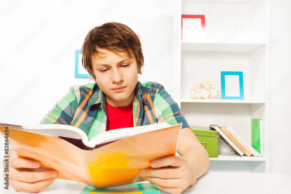 Clever boy read book sitting by table do homework