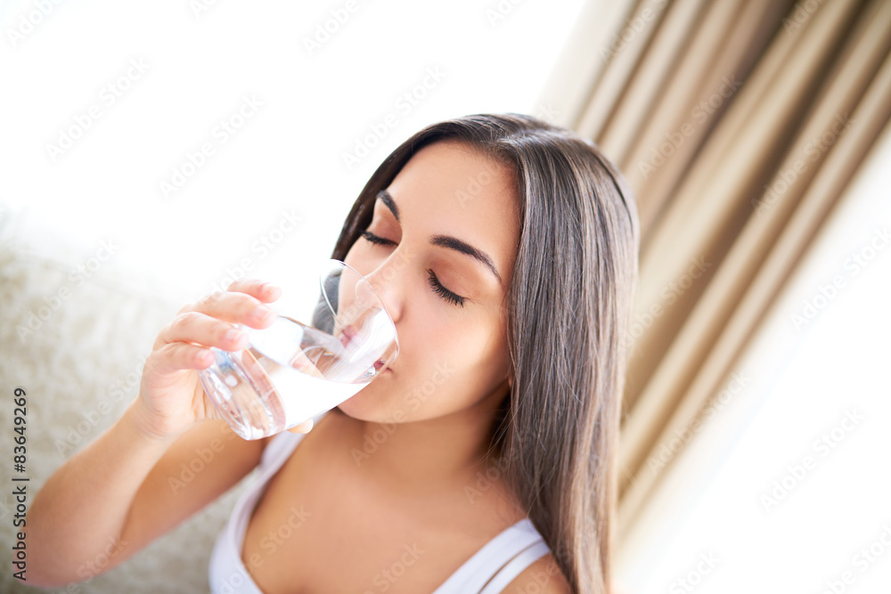 Woman drinking glass of water sitting on couch.