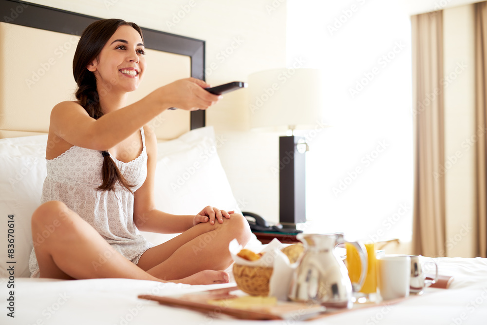 Woman relaxing in bed holding remote control.