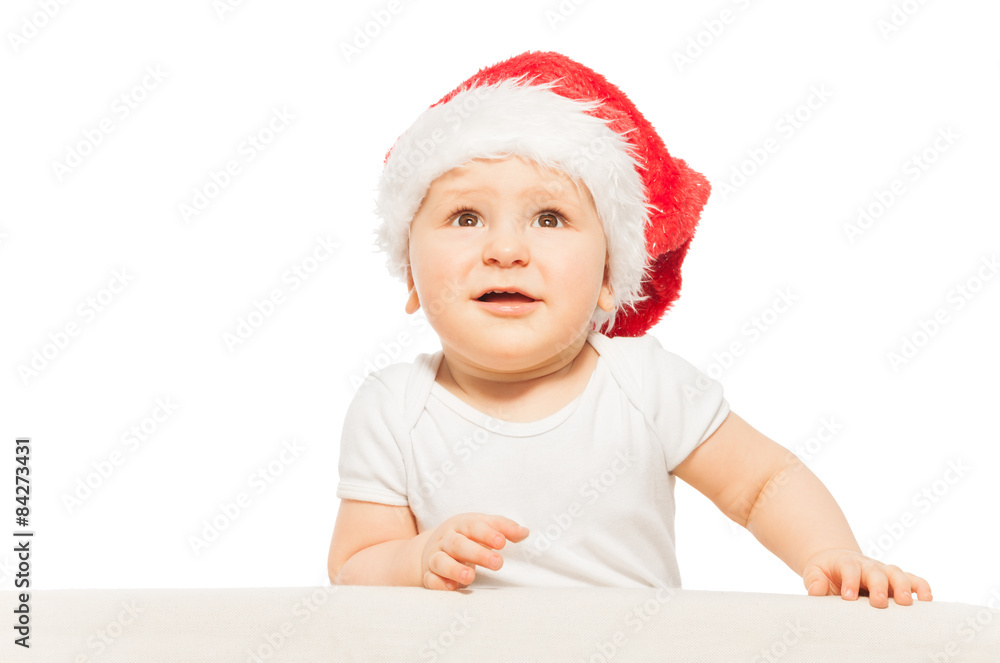 Baby in red Xmas hat looks up on white background