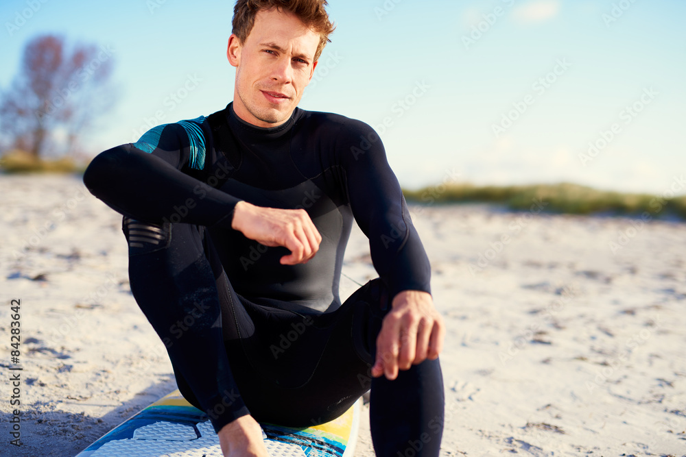 Serious young man sitting on his surfboard