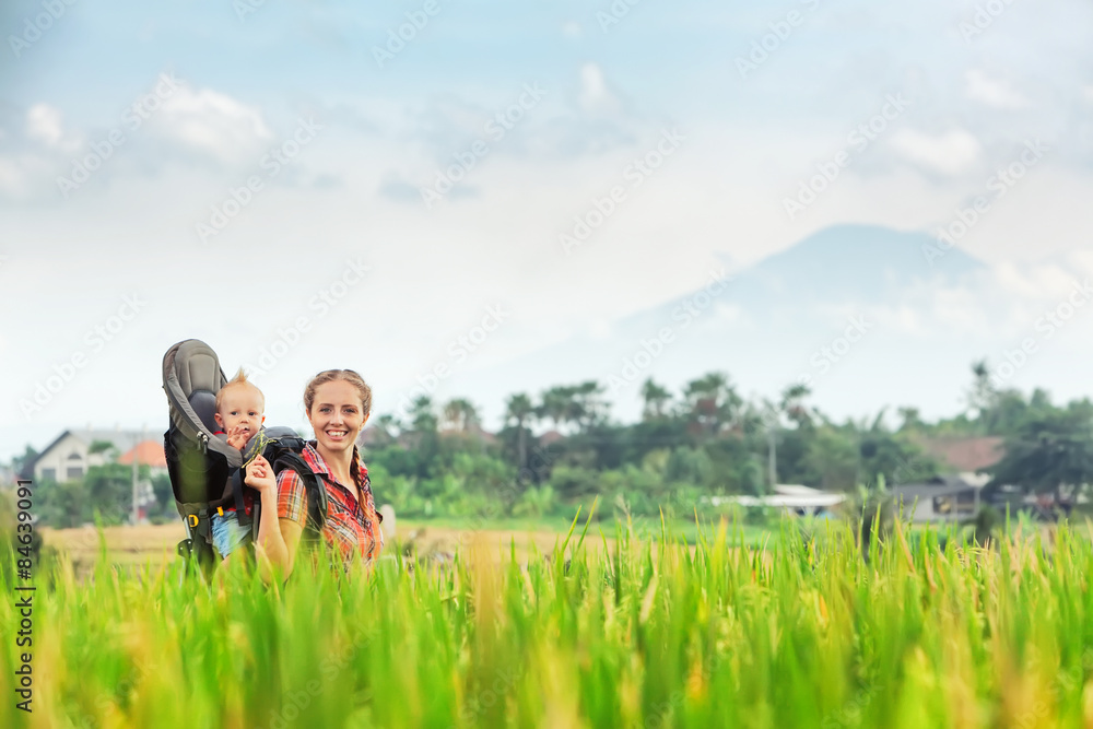 微笑的母亲背着男婴在绿色的水稻梯田上行走。带着chi旅行